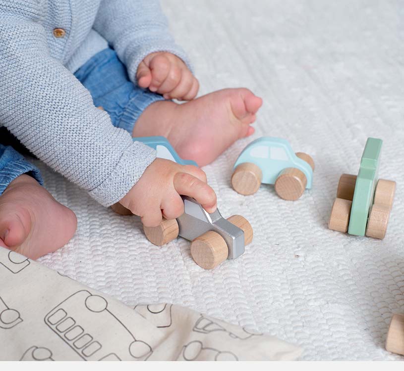 Barn leker med trelekerbiler på et hvitt teppe.