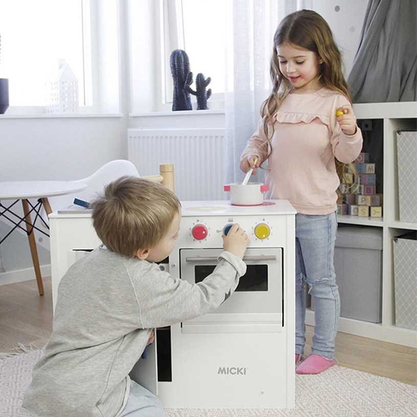 To barn leker ved en lekekomfyr i et lyst rom.