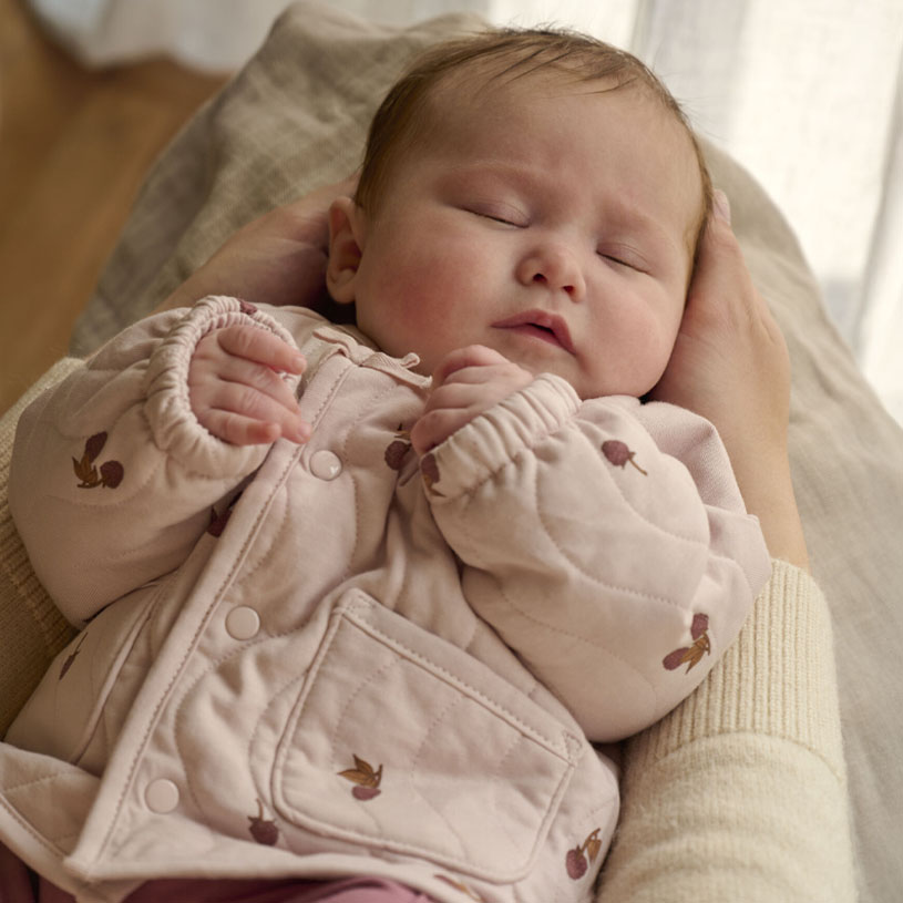 Sovende baby holdt i varme hender, klær med trykk.
