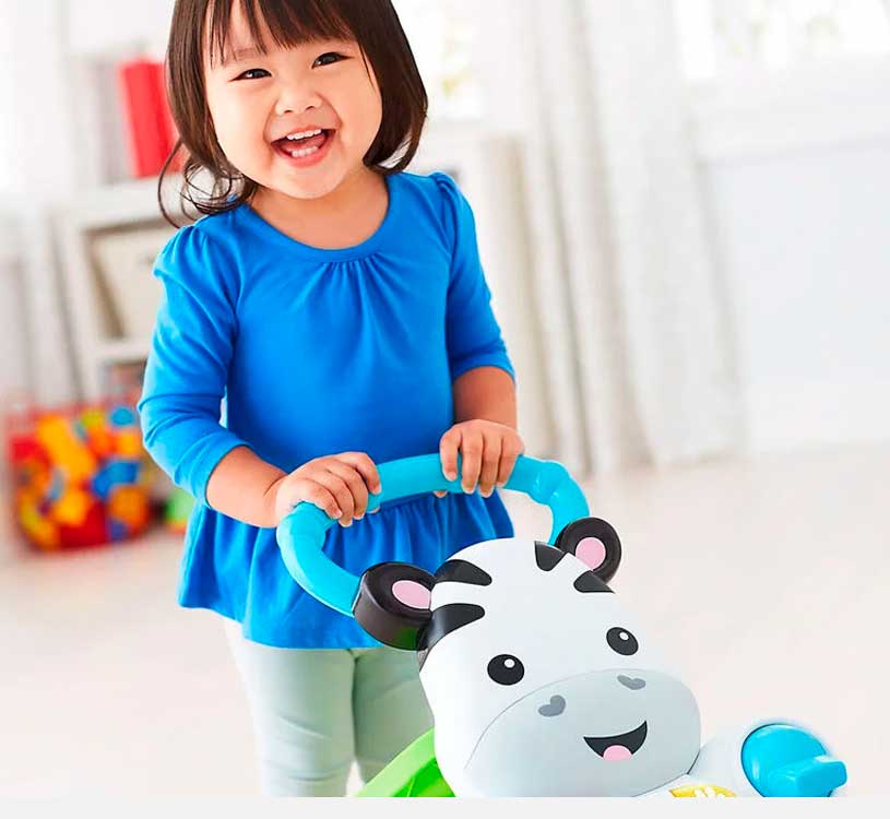 Smilende barn leker med leketøysvogn inne.