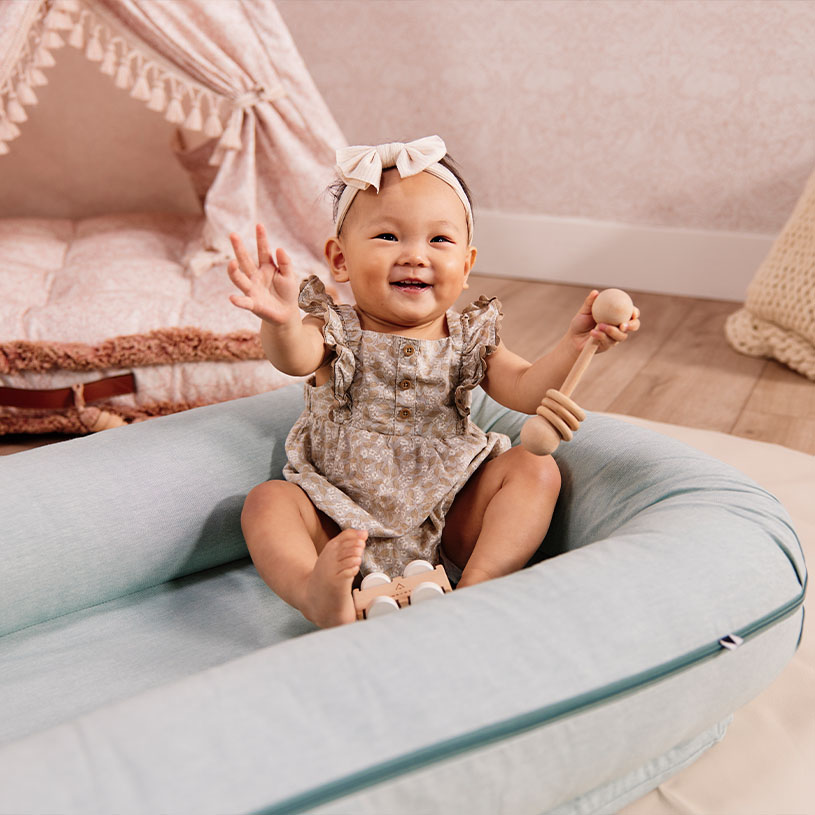 Smilende baby i blomstrete kjole med treleke i lys puteseng.