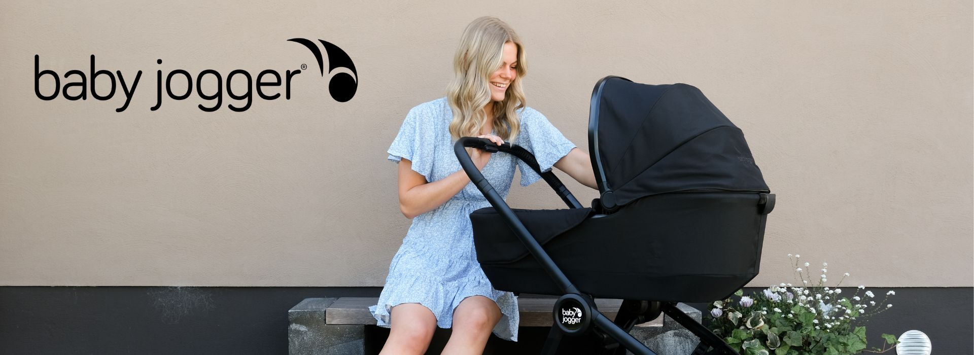 Kvinne i blå kjole sitter ved siden av en svart barnevogn fra Baby Jogger.