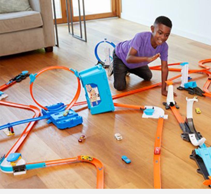 Barn leker med en leketøysbilbane og fargerike biler på tregulv.