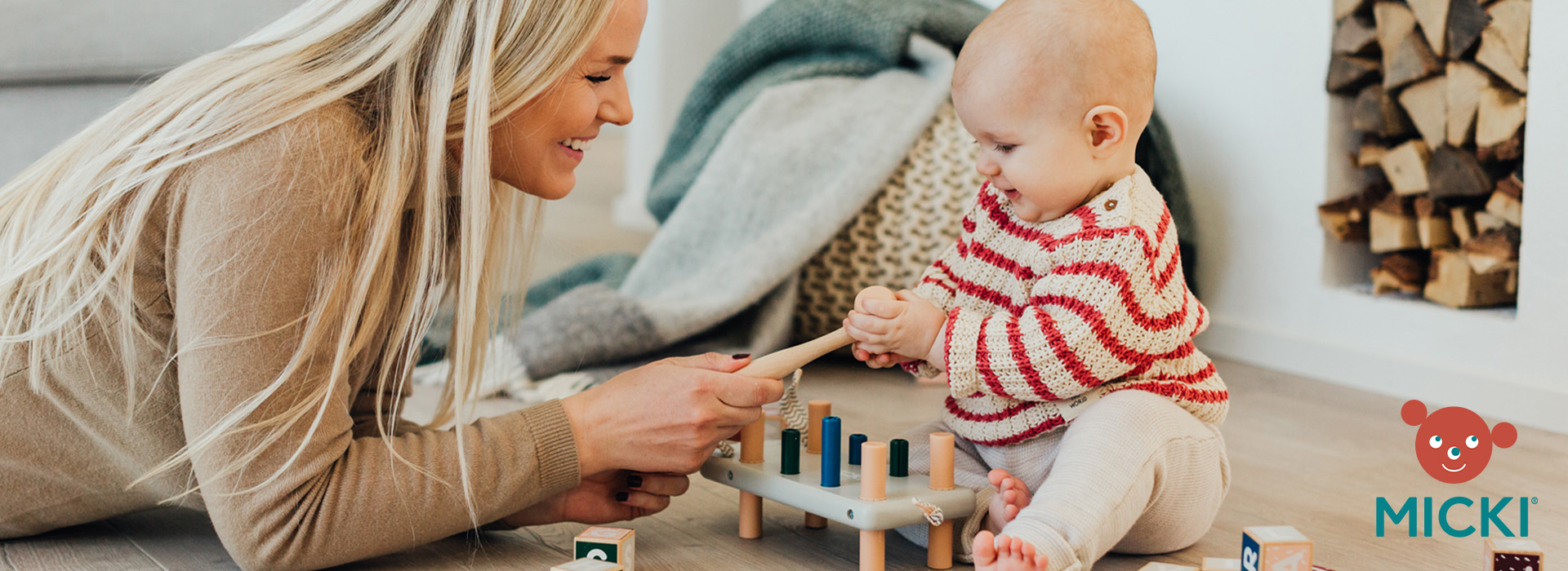 Kvinne og baby leker med et pedagogisk treleke på gulvet.