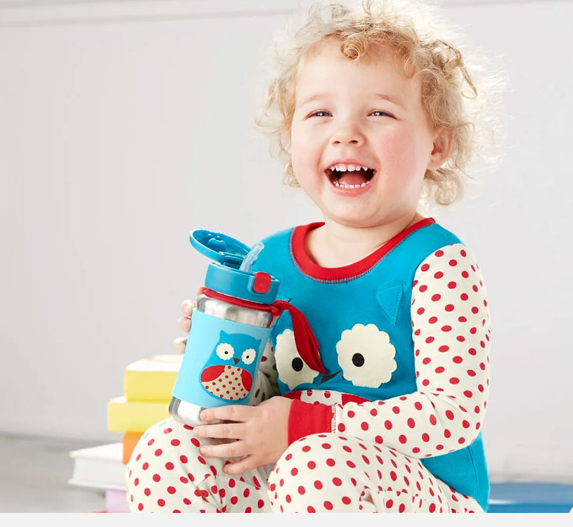 Smilende barn i prikkete pyjamas med flaske.