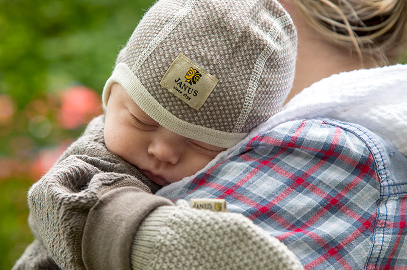 Baby sover i en voksens armer utendørs.