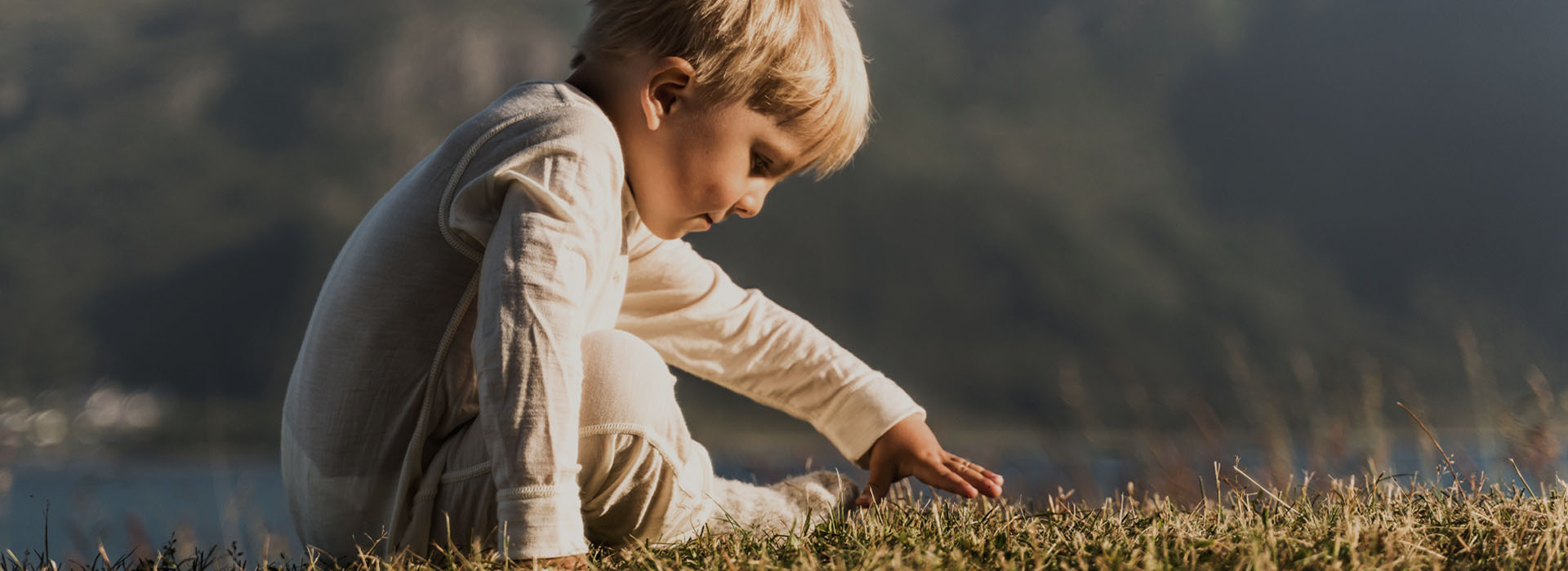 Liten gutt i hvit pyjamas leker på en gressplen i naturen.