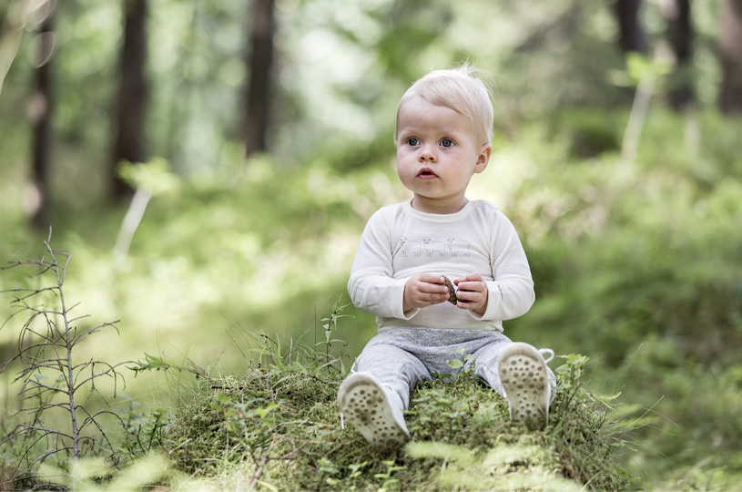 Baby sitter på en mosegrodd stubbe i skogen.