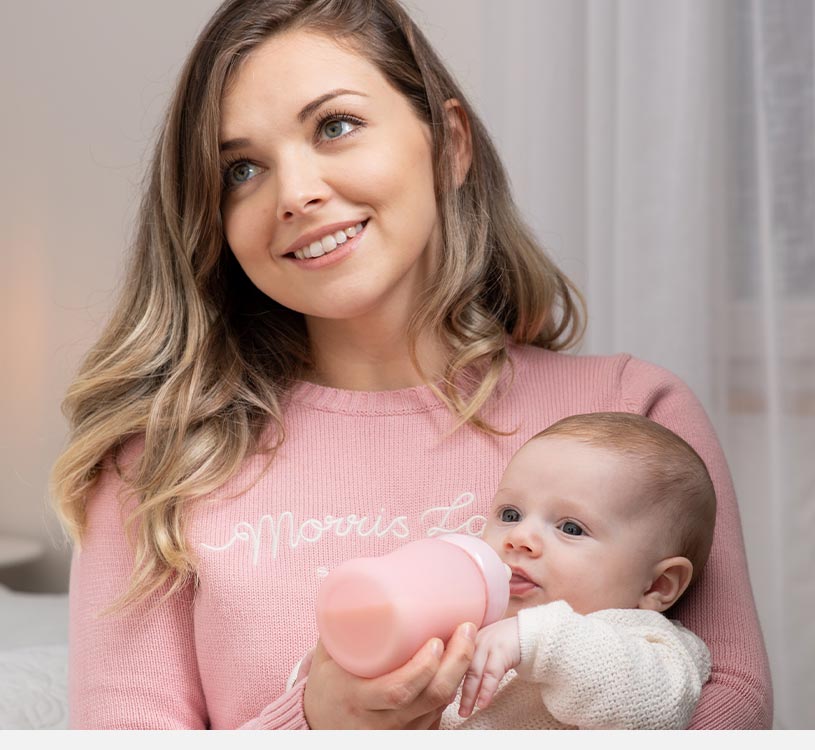 Kvinne i rosa genser mater baby med rosa flaske.
