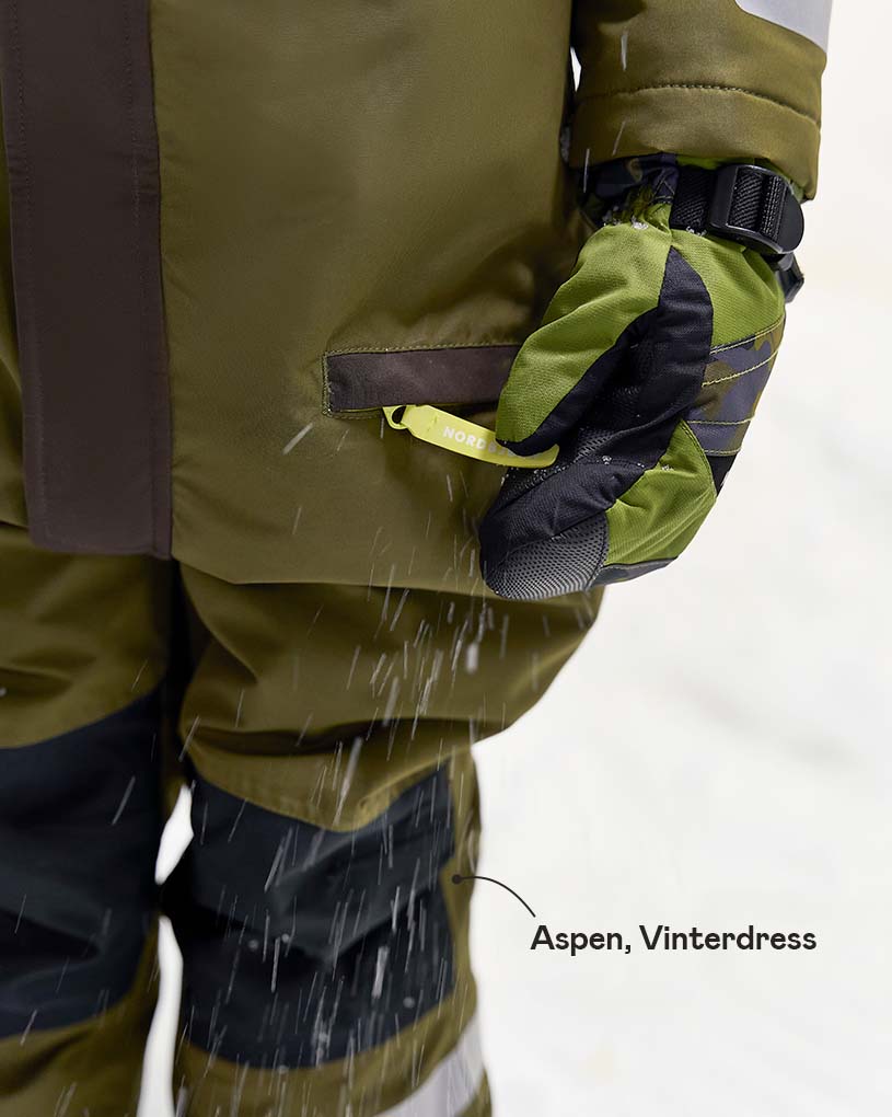 Nærbilde av en person i grønn vinterdress med snøfall.