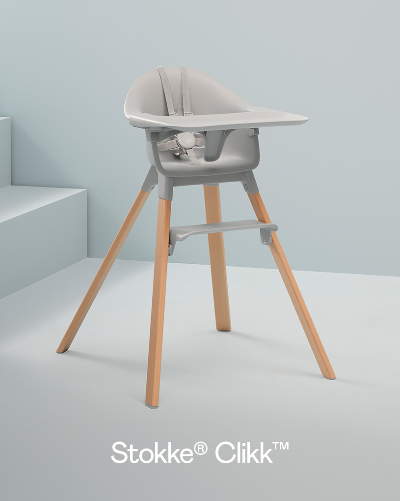 Grå barnestol med trebena og sikkerhetsbelte mot lys bakgrunn.