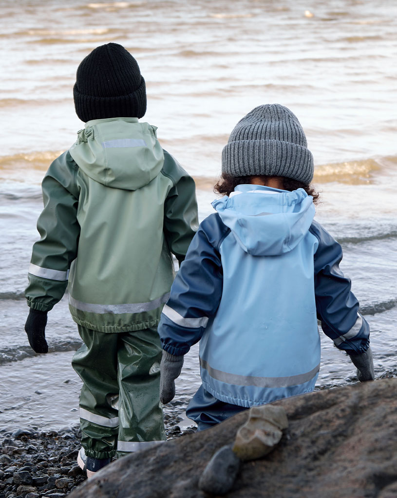 To barn i regntøy leker i vannet ved en strand.