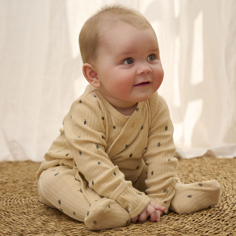 Baby i beige pyjamas sitter på teppe.