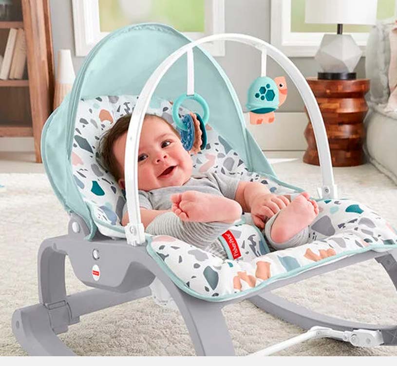 Baby i vippestol med lekebøyle i lyst rom.