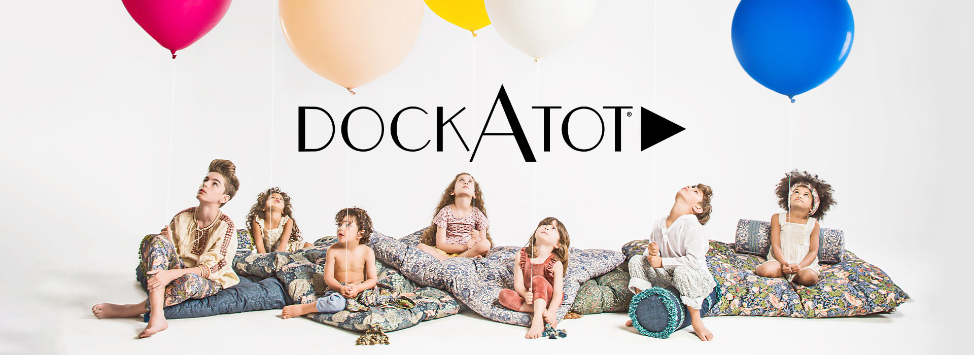 Barn sitter på puter med ballonger og DockATot-logo over.