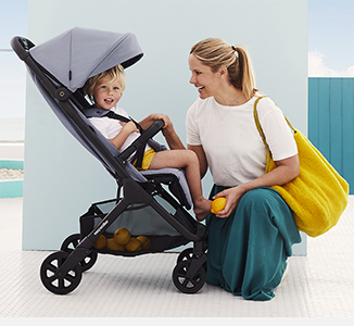 Kvinne med gul veske ved barnevogn med smilende barn.