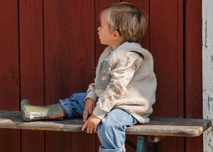 Barn sitter på en benk iført vest og gummistøvler, med teksten 'Kenza X Viking'.