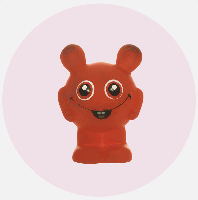Rød leketøysfigur med store øyne og smil på lys rosa bakgrunn.
