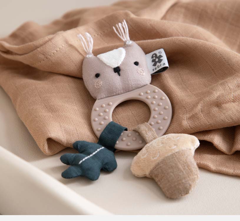 Babyleke med ugle på beige stoff.