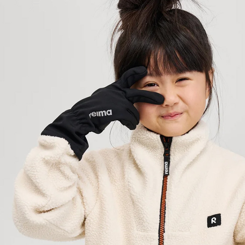 Lite barn med brun lue holder hånden foran munnen og smiler.