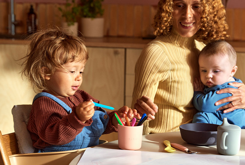 Barn tegner ved bordet, kvinne holder baby.
