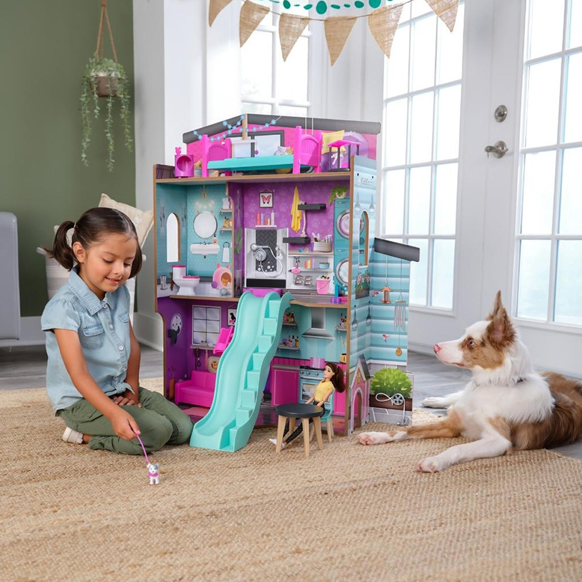 Jente og hund leker ved et dukkehus på gulvet.