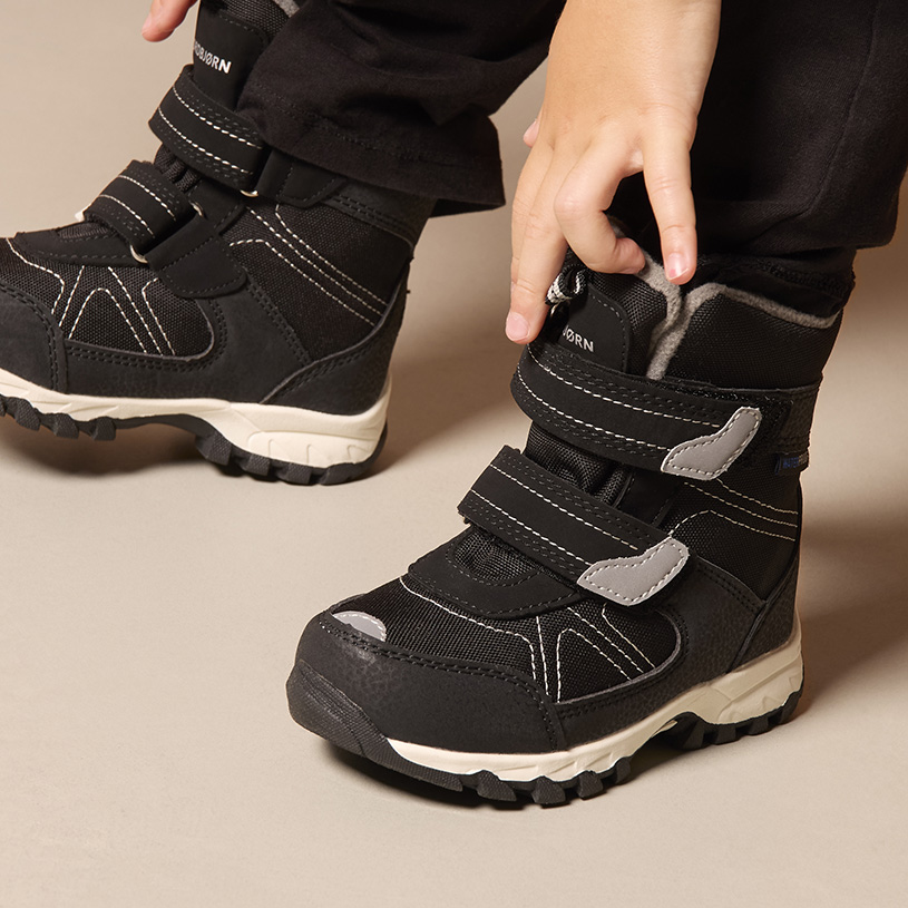 Barnehånd tar på beige støvel med borrelås.