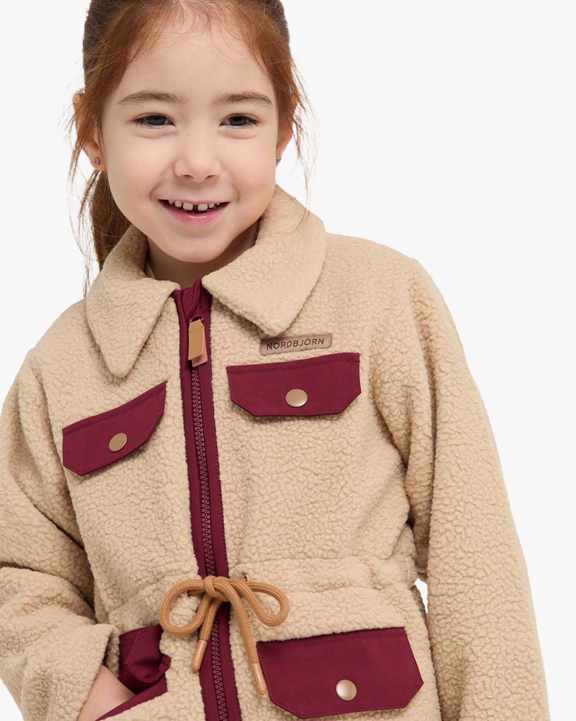 Smilende person med fletter i hvit fleecejakke ute.