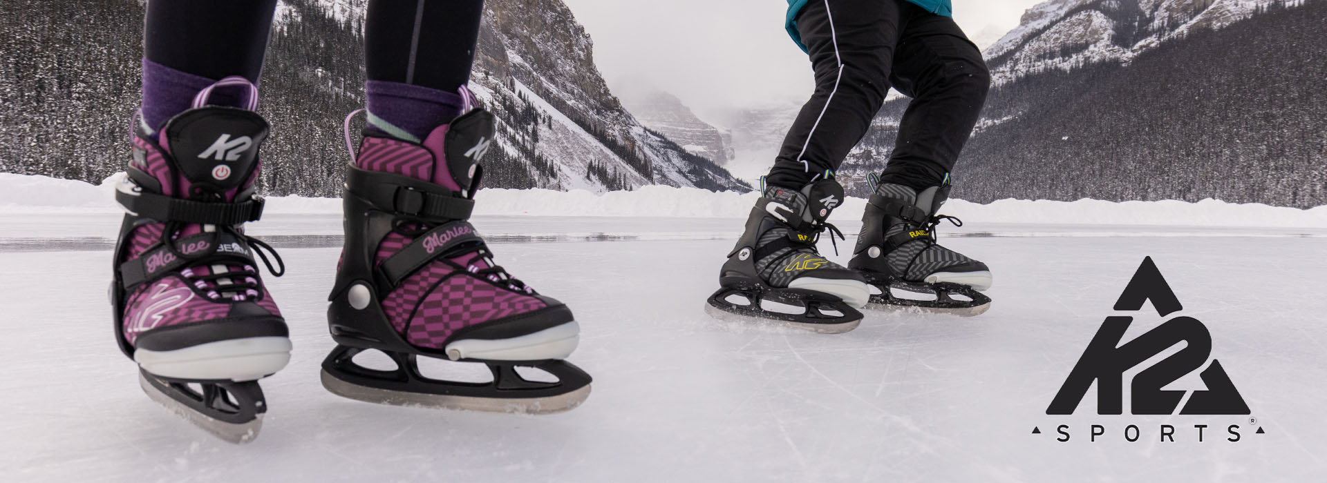 To personer går på skøyter på en frosset innsjø omgitt av fjell.