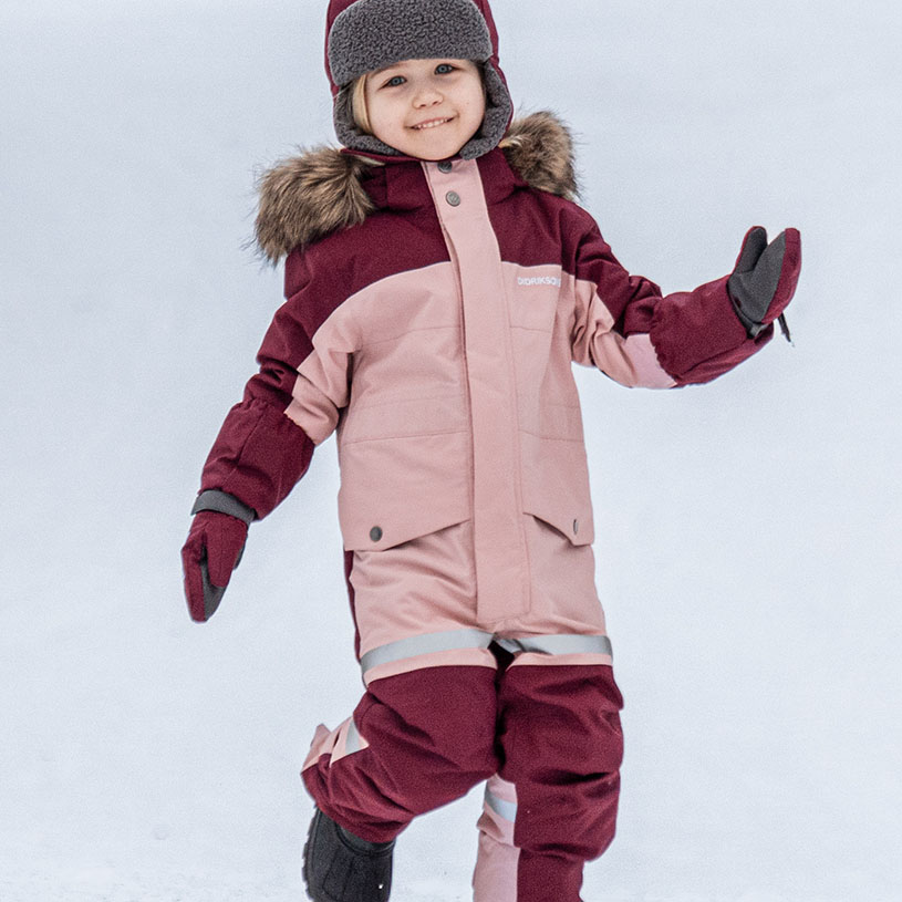 Barn i vinterdress og lue leker i snøen.