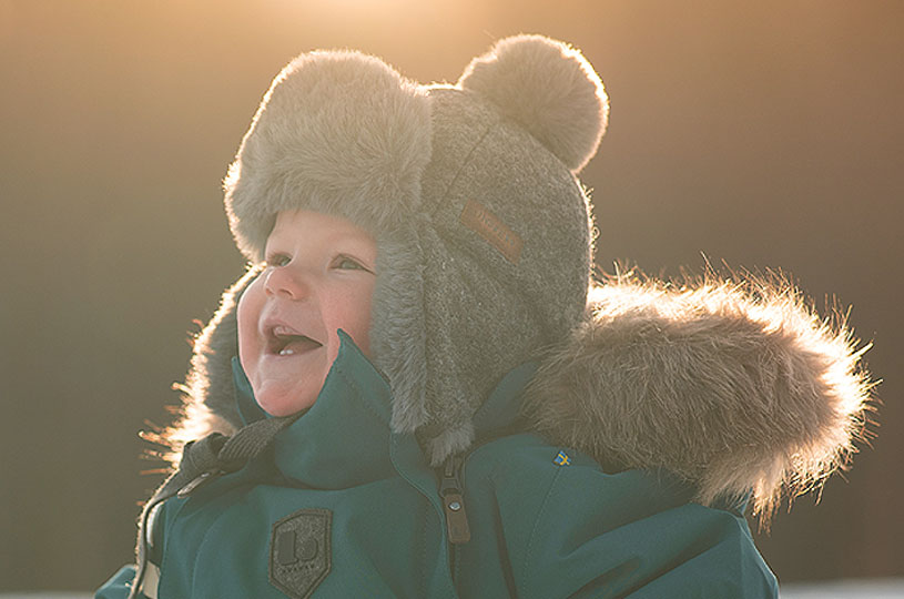 Smilende barn med tykk vinterlue i solnedgangsbakgrunn.