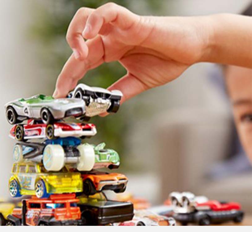 En hånd stabler lekebiler oppå hverandre.