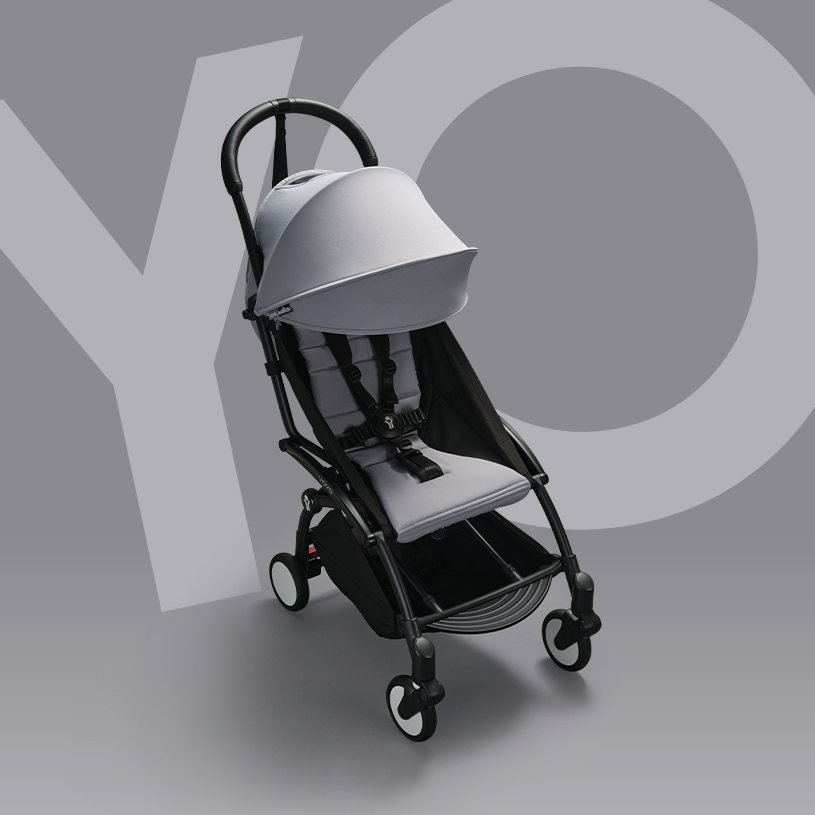 Grå barnevogn med kalesje og justerbart håndtak mot grå bakgrunn.