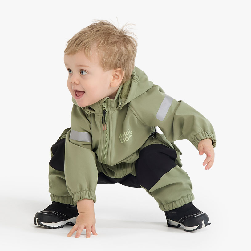 Baby i flerfarget dress med hette, sitter på hvit bakgrunn.