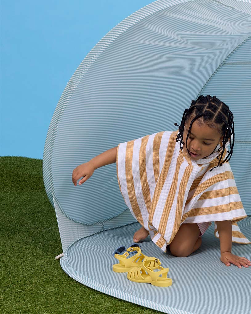To barn leker i et strandtelt på sandstrand, tekst: 'Nyhet!'.