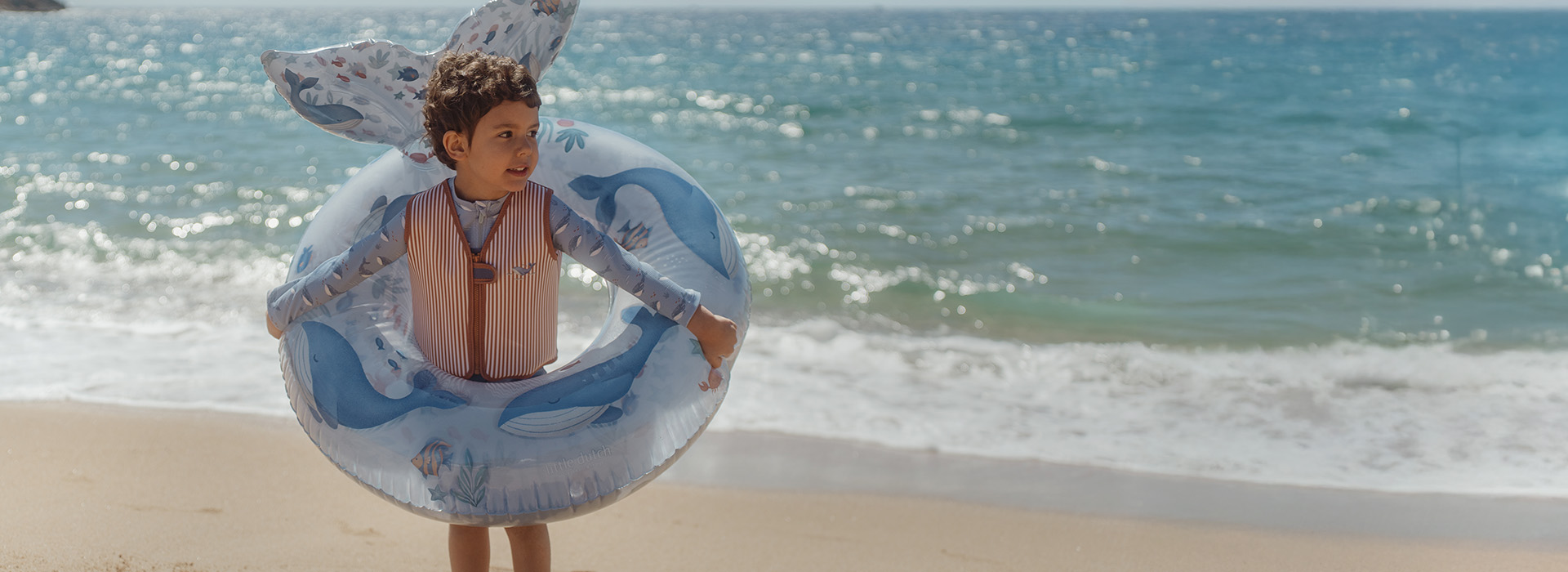 Barn på strand med badering, hav bak. Tekst: "Nytt for sesongen".