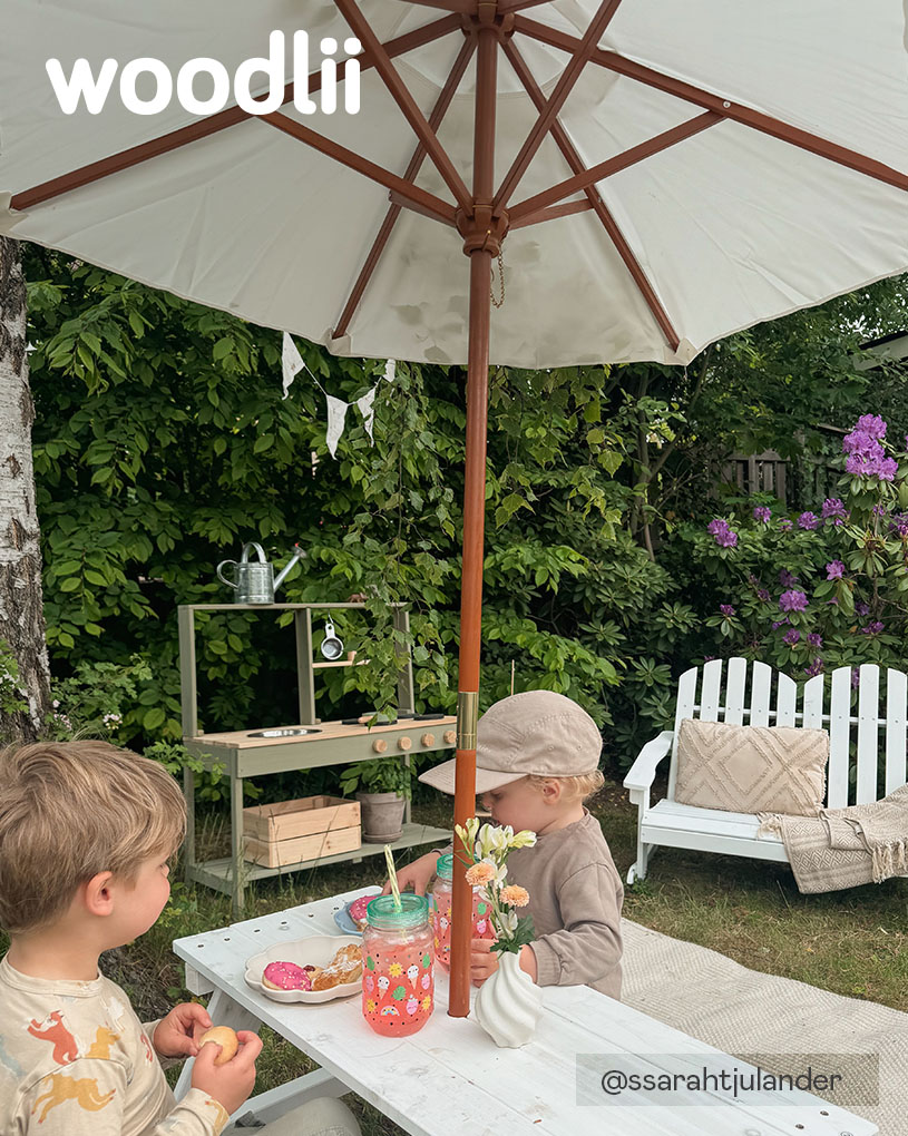 To barn sitter ved et bord under en parasoll med teksten 'woodlii'.
