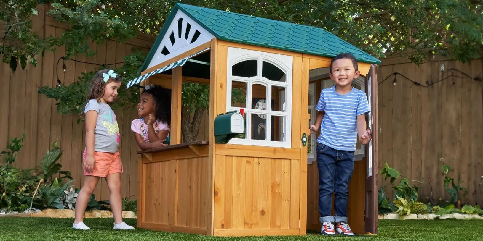 Tre barn leker ved et lite trelekestue i en hage.