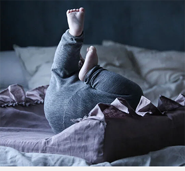 Baby i grå klær ligger på ryggen i en seng.