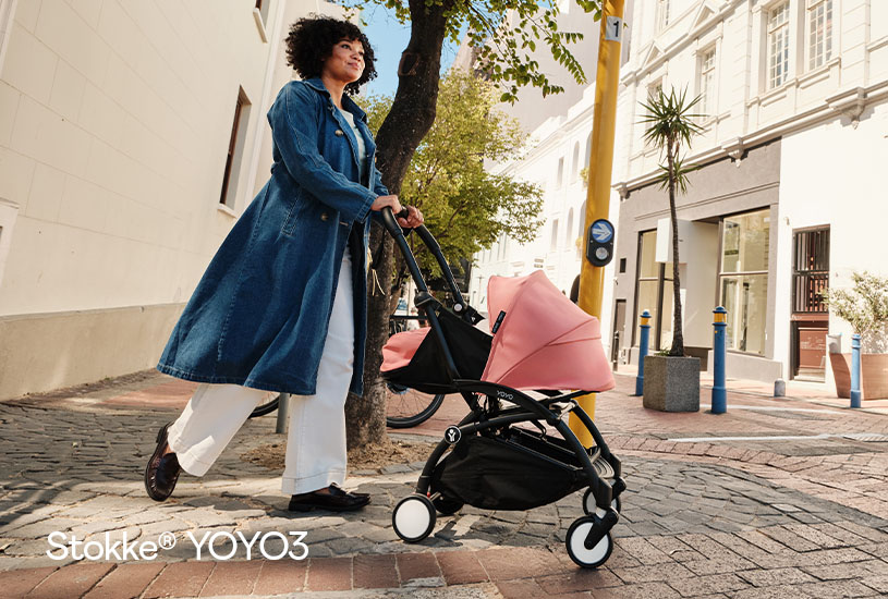 Person går med rosa barnevogn i bymiljø.