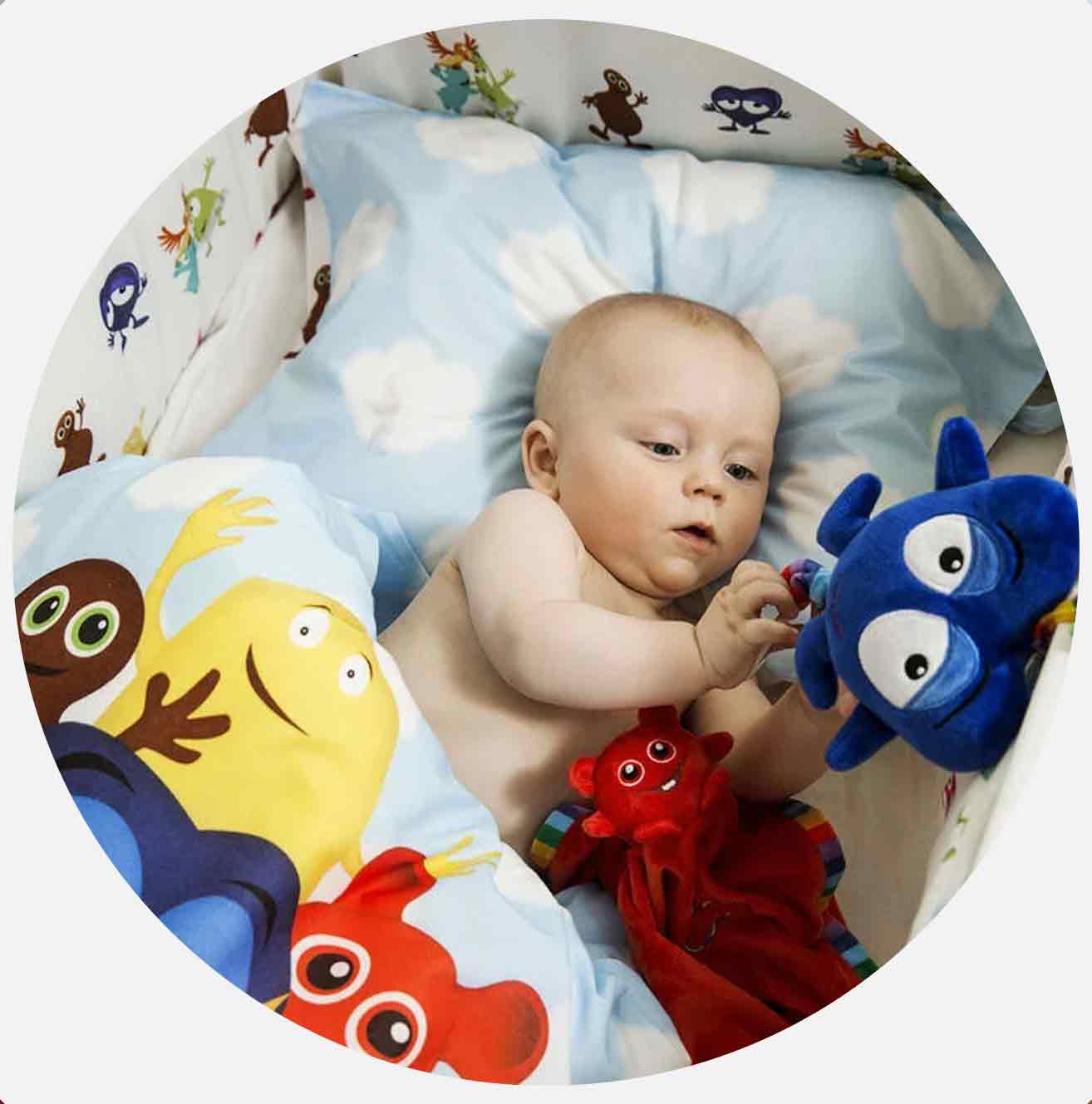 Baby leker med blått leketøy i sprinkelseng med fargerike puter.