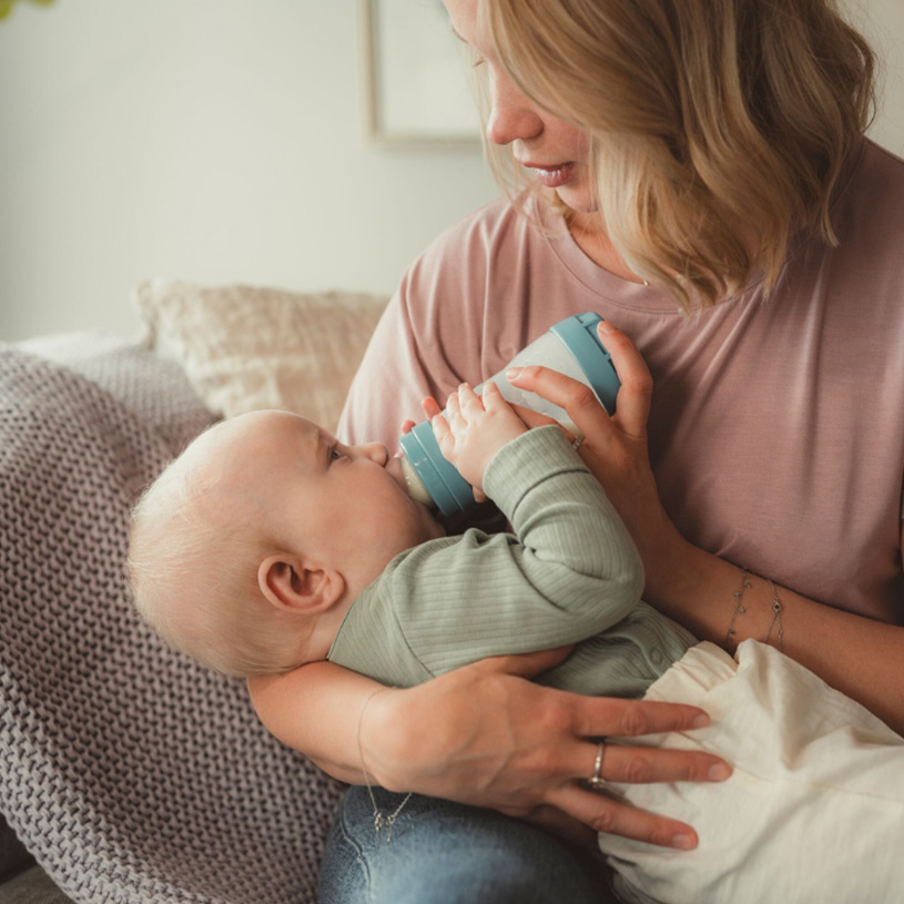 Kvinne mater baby med flaske i fanget.