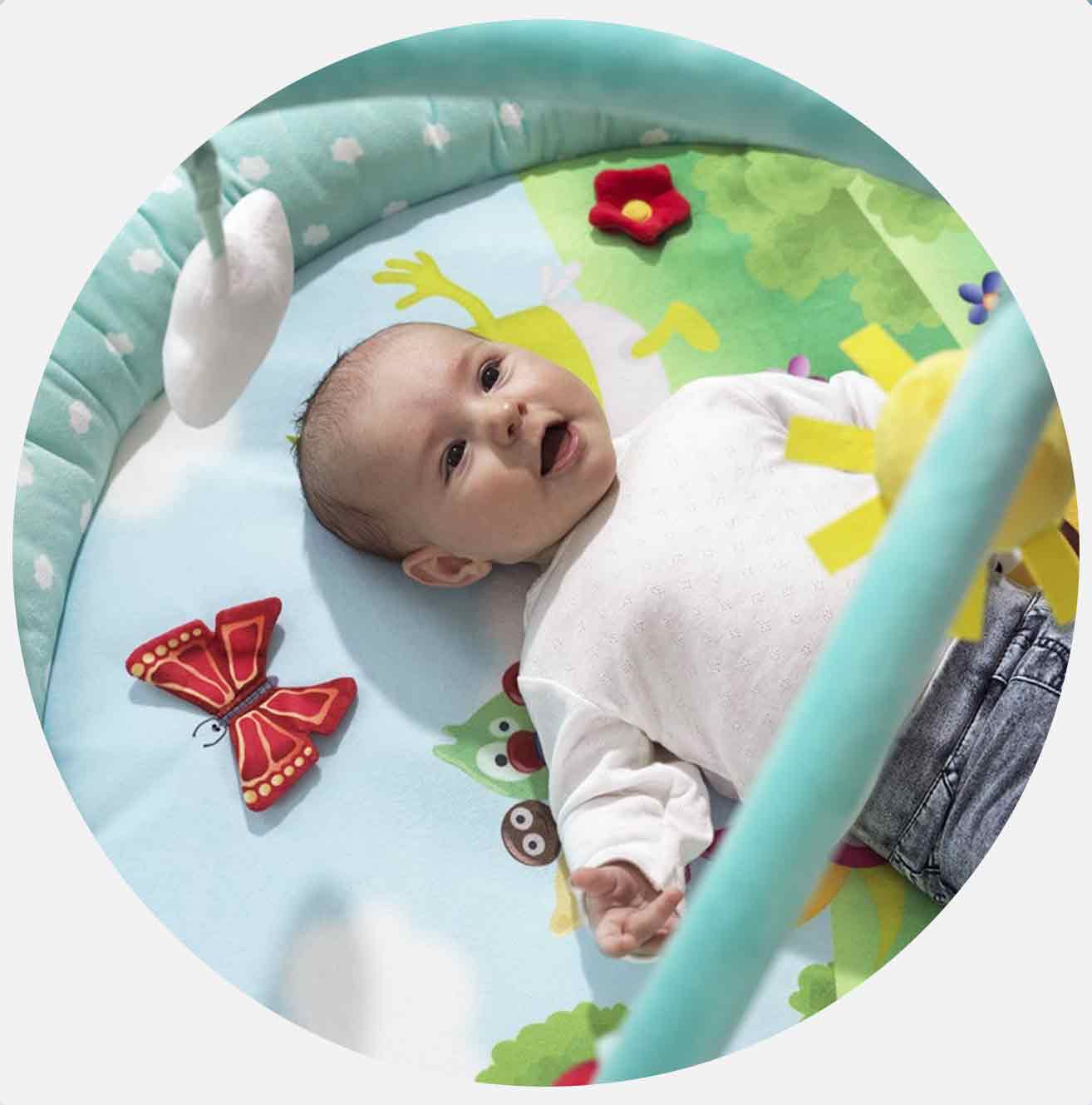 Baby ligger på fargerikt lekematte med blomster og sommerfugl.