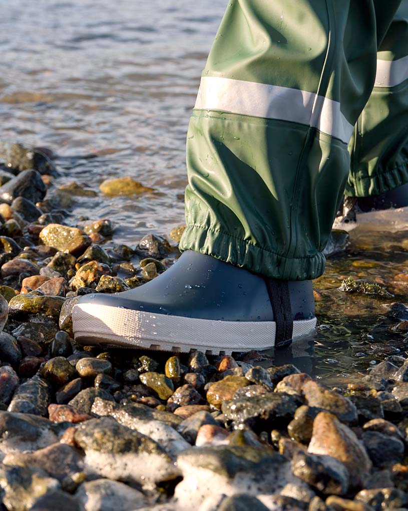 Barn i blått regntøy og rosa sko går på sand.