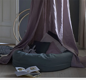 Koselig hjørne med puter og kaniner under et lilla baldakin.