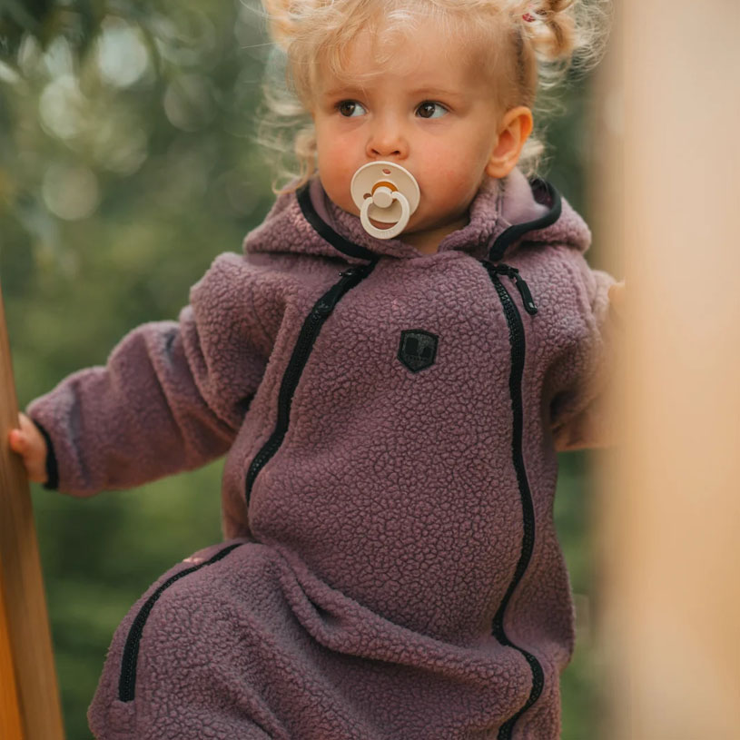Baby i rosa klær husker og smiler i en blå huske utendørs.