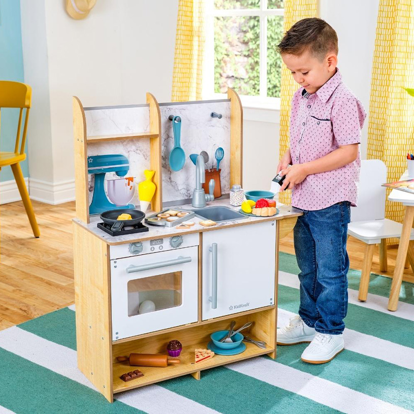 Gutt leker med lekekjøkken og lekemat i et fargerikt rom.