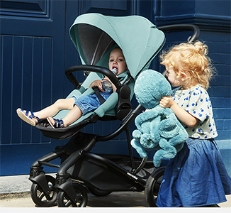 To barn, ett i barnevogn og ett med leke, foran en blå dør.