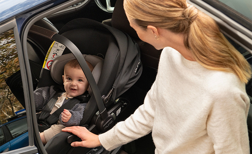 Kvinne ser på baby i bilsete, trygt festet i baksetet på bilen.