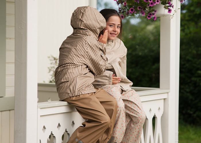 To barn sitter på en balkong og hvisker til hverandre, med teksten 'Kenza X Viking'.